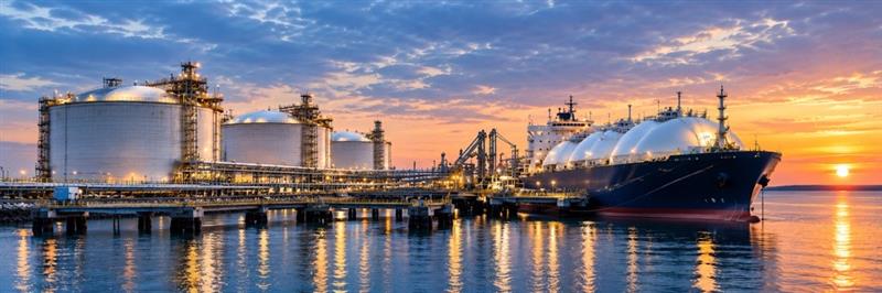 An LNG export terminal at sunset, with storage tanks and a tanker at berth